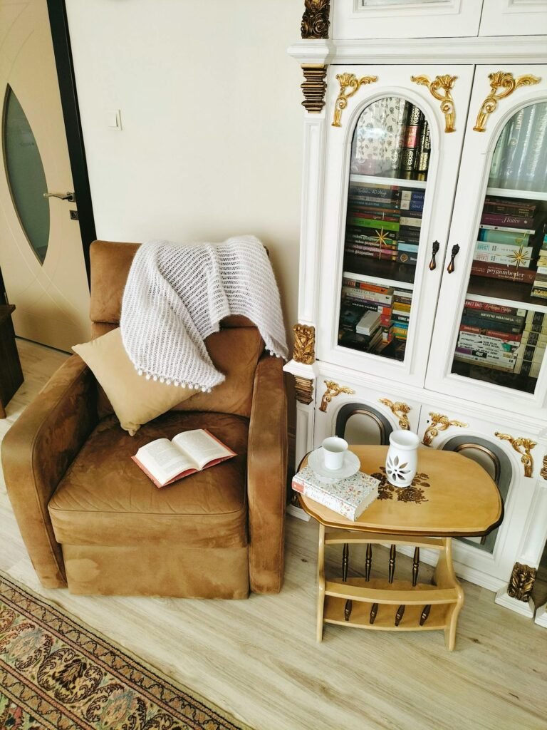 Cantinho de leitura aconchegante: poltrona marrom, manta, livro aberto e estante de livros ao fundo